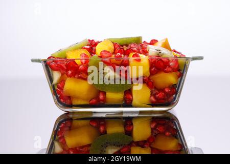 Frutta tagliata mista disposta in una ciotola trasparente di vetro con fondo bianco, isolata. Foto Stock