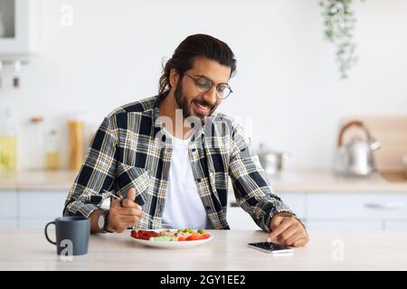 Bell'uomo indiano che usa il cellulare mentre fa colazione Foto Stock
