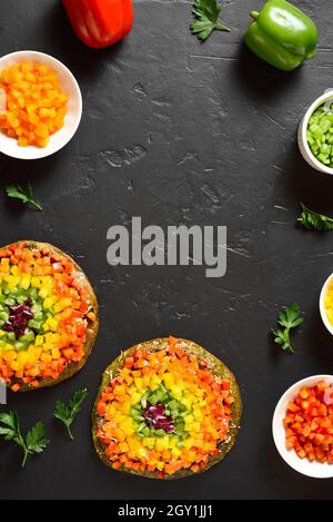 Telaio di pizza arcobaleno veggie peperoni e ingredienti su sfondo di pietra nera. Vegetariano vegano o cibo sano concetto. Vista dall'alto, piatto Foto Stock