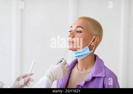 Medico che fa il test di PCR covid-19 per la paziente femminile, spazio libero. Giovane donna sottoposta a procedura diagnostica coronavirus Foto Stock