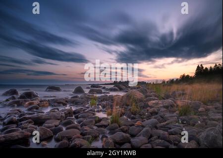 Lunga esposizione di un magnifico tramonto morbido e colorato vicino alla pietra del mare. Bel movimento nube con pietre di mare. Foto Stock