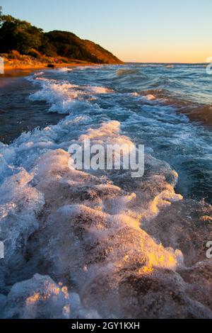 Schiumosa cresta bianca di onde si schiantano contro la spiaggia con una montagna sullo sfondo Foto Stock