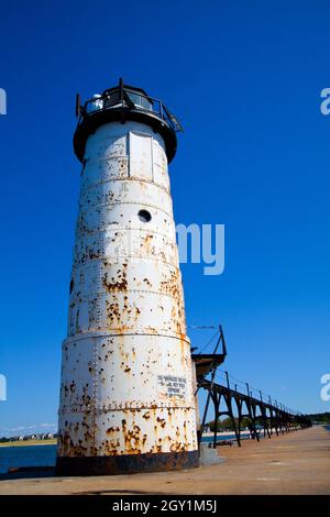 Faro bianco arrugginito alla fine di un lungo molo di legno contro un cielo blu chiaro Foto Stock