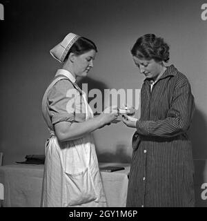 Eine junge Schwester des Deutschen Roten Kreuzes verarbreicht einer Kranken eine Tablette, Deutschland 1930er Jahre. Un giovane infermiere della Croce Rossa tedesca applicando una pillola per una donna malata, Germania 1930s. Foto Stock