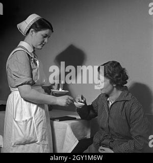 Eine junge Schwester des Deutschen Roten Kreuzes verarbreicht einer Kranken eine Tablette, Deutschland 1930er Jahre. Un giovane infermiere della Croce Rossa tedesca applicando una pillola per una donna malata, Germania 1930s. Foto Stock