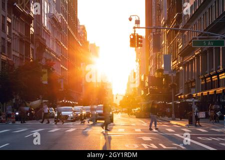 Scena stradale affollata a New York City con folle di persone che attraversano un incrocio sulla 5th Avenue con la luce di un tramonto estivo che brilla nel Foto Stock