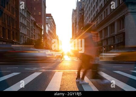 Persone e automobili che attraversano l'incrocio trafficato sulla 5th Avenue con luce del tramonto che brilla sulla 5th Avenue a Manhattan, New York City NYC Foto Stock