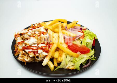 Kebab Donner con patatine e insalata, su un piatto nero isolato su sfondo bianco. Foto Stock