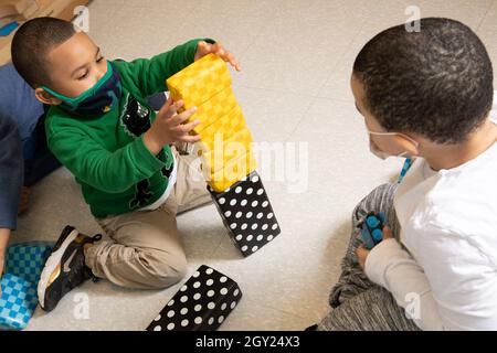 Istruzione Preschool 3-4 anni due ragazzi in blocco area giocare con blocchi colorati in schiuma blocchi, un ragazzo impilamento, mentre gli altri orologi, entrambi indossando fac Foto Stock