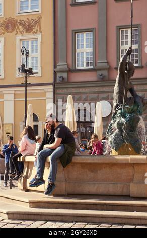 POZNAN, POLONIA - Sep 30, 2017: Un colpo di due persone seduti sulla fontana di Nettuno nella piazza della città vecchia di Poznan Foto Stock