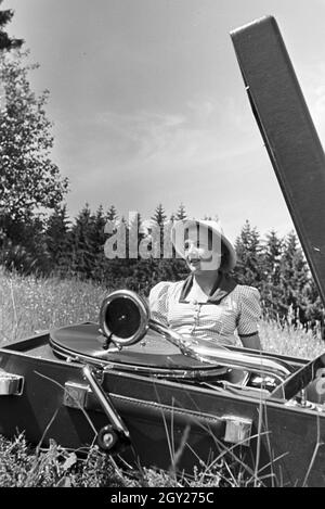 Eine junge Frau hört sich eine Platte der Schallplattenfirma Electrola mit dem Koffergrammophon auf der Wiese un, Deutschland 1930er Jahre. Una giovane donna di ascolto di un record dell'etichetta discografica Electrola giocato su un portatile wind-up gramophone, Germania 1930s. Foto Stock