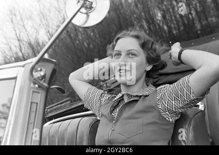 Eine junge Frau schminkt sich im Seitenspiegel ihres Cabrios, Deutschland 1930er Jahre. Una giovane donna controllando il suo make up nell'ala specchio della sua cabrio, Germania 1930s. Foto Stock