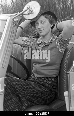 Eine junge Frau schminkt sich im Seitenspiegel ihres Cabrios, Deutschland 1930er Jahre. Una giovane donna controllando il suo make up nell'ala specchio della sua cabrio, Germania 1930s. Foto Stock