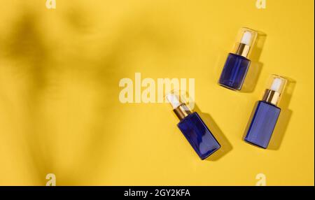 flaconi in vetro blu per cosmetici con pipetta su sfondo giallo. Cosmetici SPA mockup branding, vista dall'alto, spazio copia Foto Stock