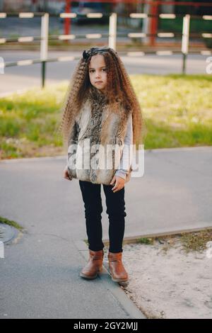 Baby girl di 4-5 anni con stivali, cappotto in pelliccia, movimento e gioco. Autunno stagione autunnale Foto Stock