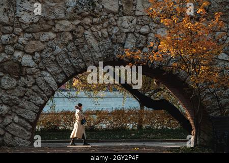 MOSCA, RUSSIA - OTTOBRE 06 2021: Una donna in un impermeabile cammina davanti ad un arco nel Parco Gorky. Foto Stock