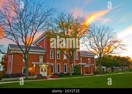 Edificio in mattoni rossi di stile coloniale con lussureggiante prato verde al tramonto Foto Stock