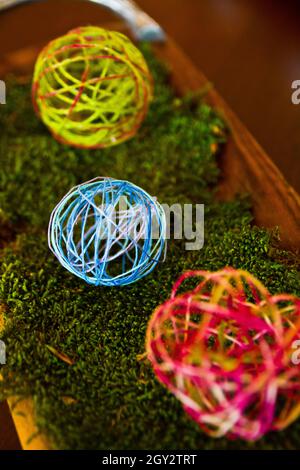 Piccole palline di filo giallo e rosso che siedono su un cestino riempito di muschio verde finto Foto Stock