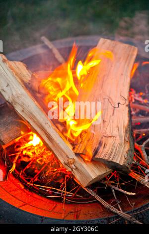 Fuoco crepuscolo in una fossa con tronchi in cima alla fiamma curling Foto Stock