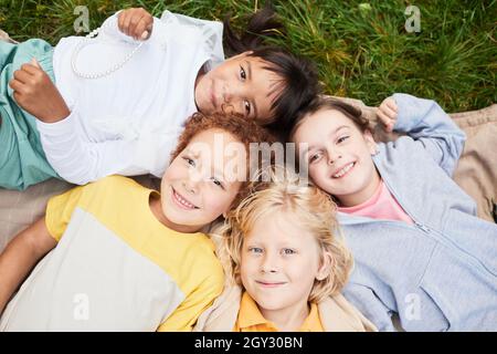 Vista dall'alto ritratto di diversi gruppi di bambini che si trovano sull'erba nel parco e guardano la macchina fotografica sorridente Foto Stock
