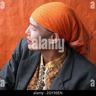 Una donna che indossa un copricapo arancione o hijab e un blazer grigio che vende peperoncini rossi in un mercato all'aperto a Bukittinggi, West Sumatra, Indonesia. Foto Stock