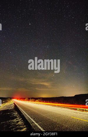 Tempo trascorso lungo esposizione shot di traffico su una strada abbandonata nel mezzo del deserto con un cielo stellato in testa Foto Stock