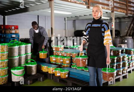 Lavoratore di sesso femminile che le scorte di contenitori di plastica e lattine con olive in magazzino Foto Stock
