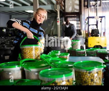 Lavoratore di sesso femminile che le scorte di contenitori di plastica e lattine con olive in magazzino Foto Stock