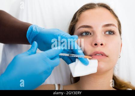 Primo piano faccia della giovane donna che riceve le iniezioni durante la procedura di miglioramento del labbro Foto Stock