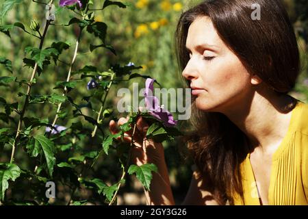 Attraente giovane spagnola donna che odora fresco viola ibisco fiore in un parco Foto Stock