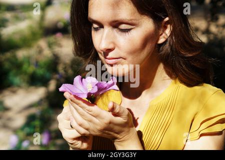 Attraente giovane spagnola donna che odora fresco viola ibisco fiore in un parco Foto Stock