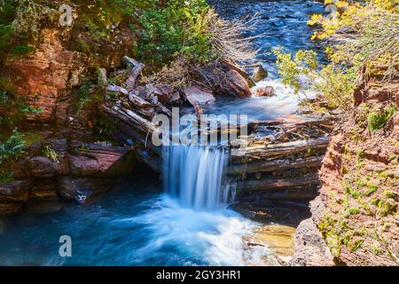 Cascata che scorre su barricata di tronchi in canyon Foto Stock