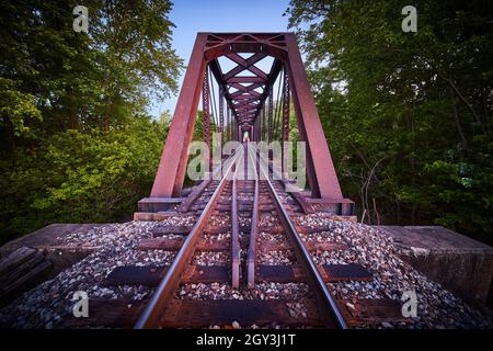 Ampia vista sui binari con ponte industriale e treno alla fine in avvicinamento Foto Stock