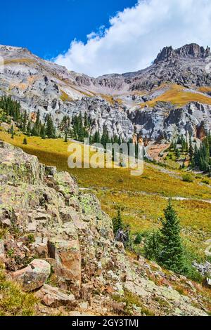Vista aperta nella valle di montagna di cime grigie di montagna con pini e grandi rocce ricoperte di lichen da vicino Foto Stock