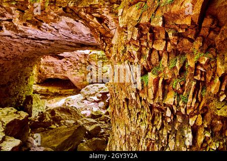 Colonna della grotta di pezzi di roccia ricoperti di muschio con apertura della grotta sullo sfondo Foto Stock