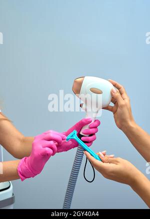 Una donna sintonizza una macchina per la rimozione dei capelli al laser. Tiene una parte funzionante dell'epilatore nelle mani e si pone per una foto. Si trova in un moderno bea Foto Stock