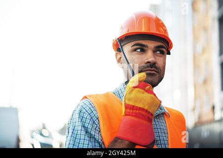 Giovane lavoratore di costruzione in uniforme utilizzando walkie talkie in loco Foto Stock