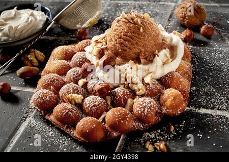 Cialda tradizionale a bolle d'aria con gelato alla noce e noci fresche o noci pecan e nocciole su panna montata cosparso di zucchero in un clo ad angolo alto Foto Stock