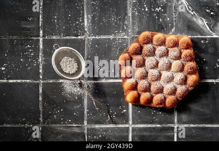 Alla moda croccante bolla d'oro o waffle all'uovo cosparsi di zucchero a velo in una vista dall'alto su piastrelle grigio scuro con copyspace Foto Stock