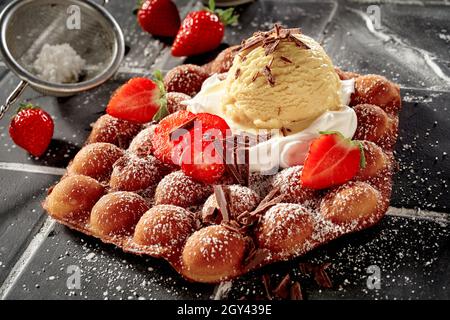 Gourmet Bubble waffle dessert estivo con fragole fresche, panna montata e gelato alla frutta con cioccolato fiocchi e zucchero a velo Foto Stock