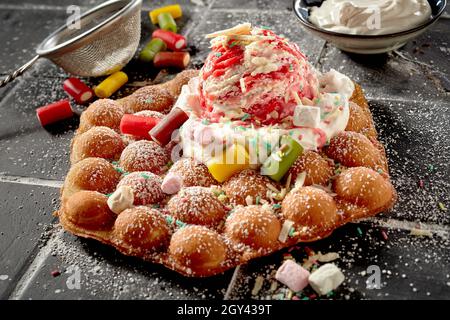 Festeggiate con cialde a bolle d'aria e dessert a caramelle conditi con panna montata e un cucchiaio di gelato variegato fruttato in una vista ad angolo alto per l'annuncio del menu Foto Stock