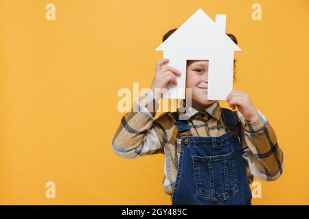 Ragazza di capretto giocoso graziosa che tiene la casa di carta, l'alloggiamento senza tetto e concetto di assicurazione di protezione della casa, giorno internazionale delle famiglie, la cura domestica di incoraggiamento Foto Stock