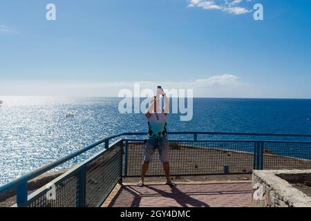 Insoddisfatto, giovane ragazzo maschio turista fa un selfie sullo sfondo del mare. Un uomo viaggia facendo foto sul suo smartphone mobile. turista con un Foto Stock
