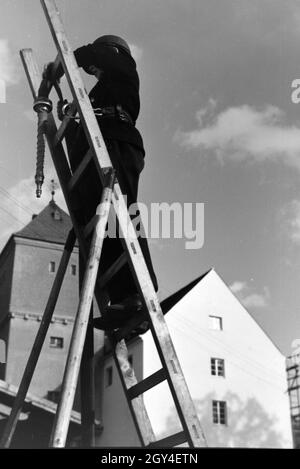 Ein Junge von der Kinderfeuerwehr bei einer Feuerwehrübung mit dem Löschschlauch auf einer Leiter, Deutschland 1930er Jahre. Un ragazzo della junior vigili del fuoco in piedi su una scala con il tubo flessibile di acqua durante un vigile del fuoco di formazione, Germania 1930s. Foto Stock