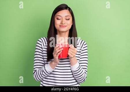 Foto di gioioso brunette giovane signora odore tè indossare camicia bianca isolato su sfondo verde Foto Stock