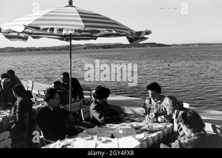 Gäste eines Café am Chiemsee sitzen unter Sonnenschirmen auf der Terrasse, Deutschland 1930 Jahre. Come ospiti di una caffetteria del Chiemsee, sdraiato sotto le ombre del sole sulla terrazza, la Germania degli anni trenta. Foto Stock