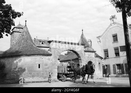 Ein kleiner Junge beobachtet wie eine Pferdekutsche beladene durch das Burgtor a Rothenburg ob der Tauber fährt, Deutschland 1930er Jahre. Un ragazzino sta guardando un caricato una carrozza a cavalli di guida attraverso la porta del castello a Rothenburg ob der Tauber, Germania 1930s. Foto Stock