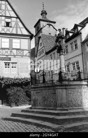 Ein Springbrunnen mit einer kleinen statua in Rothenburg ob der Tauber, von der dem gotische Teil mitsamt hohem Turm im Hintergrund sichtbar Ist Deutschland 1930er Jahre. Una fontana con una piccola statua in Rothenburg ob der Tauber, con il gotico e la parte alta towerin sullo sfondo, Germania 1930s. Foto Stock