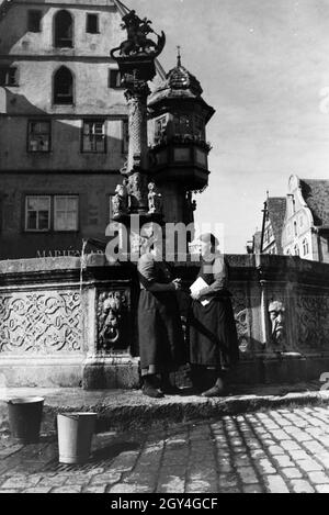 Zwei Frauen unterhalten sich während Sie die Wassereimer mit Wasser aus dem Springbrunnen vor dem imposanten Rathaus voll laufen lassen, Rothenburg ob der Tauber, Deutschland 1930er Jahre. Due donne aventi una chat mentre il bucktes sono il riempimento con acqua dalla fontana posta di fronte all'imponente Municipio di Rothenburg ob der Tauber, Germania 1930s. Foto Stock