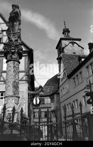 Ein Springbrunnen mit einer kleinen statua in Rothenburg ob der Tauber, von der dem gotische Teil mitsamt hohem Turm im Hintergrund sichtbar Ist Deutschland 1930er Jahre. Una fontana con una piccola statua in Rothenburg ob der Tauber, con il gotico e la parte alta towerin sullo sfondo, Germania 1930s. Foto Stock